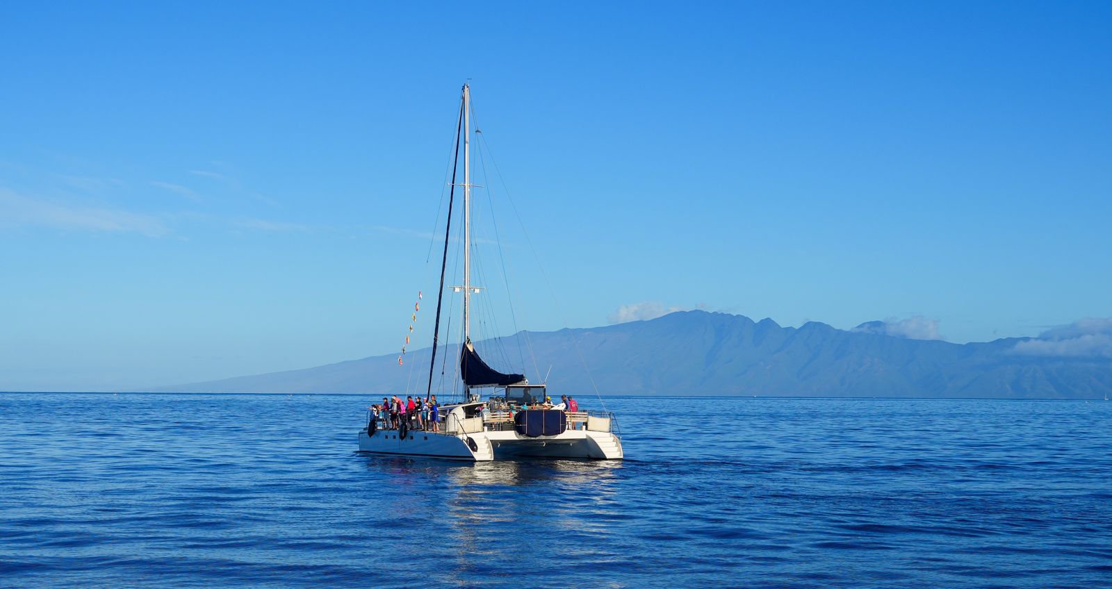 A white catamaran on blue water with Maui's mountains behind