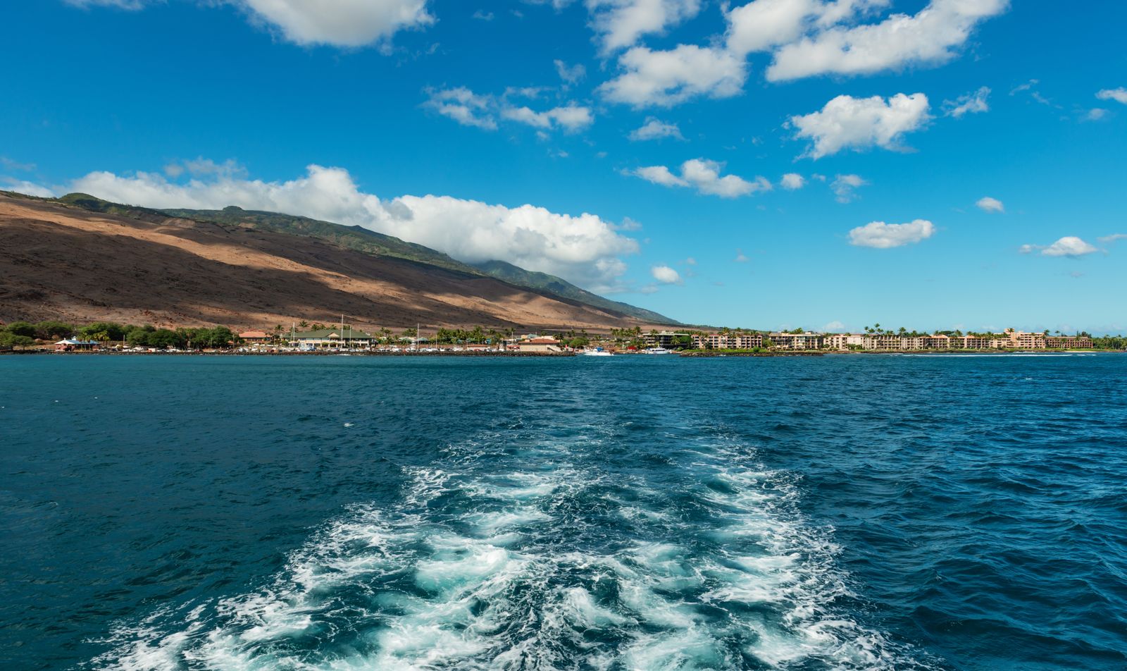 A boat's white wake leaving the Maui coast behind